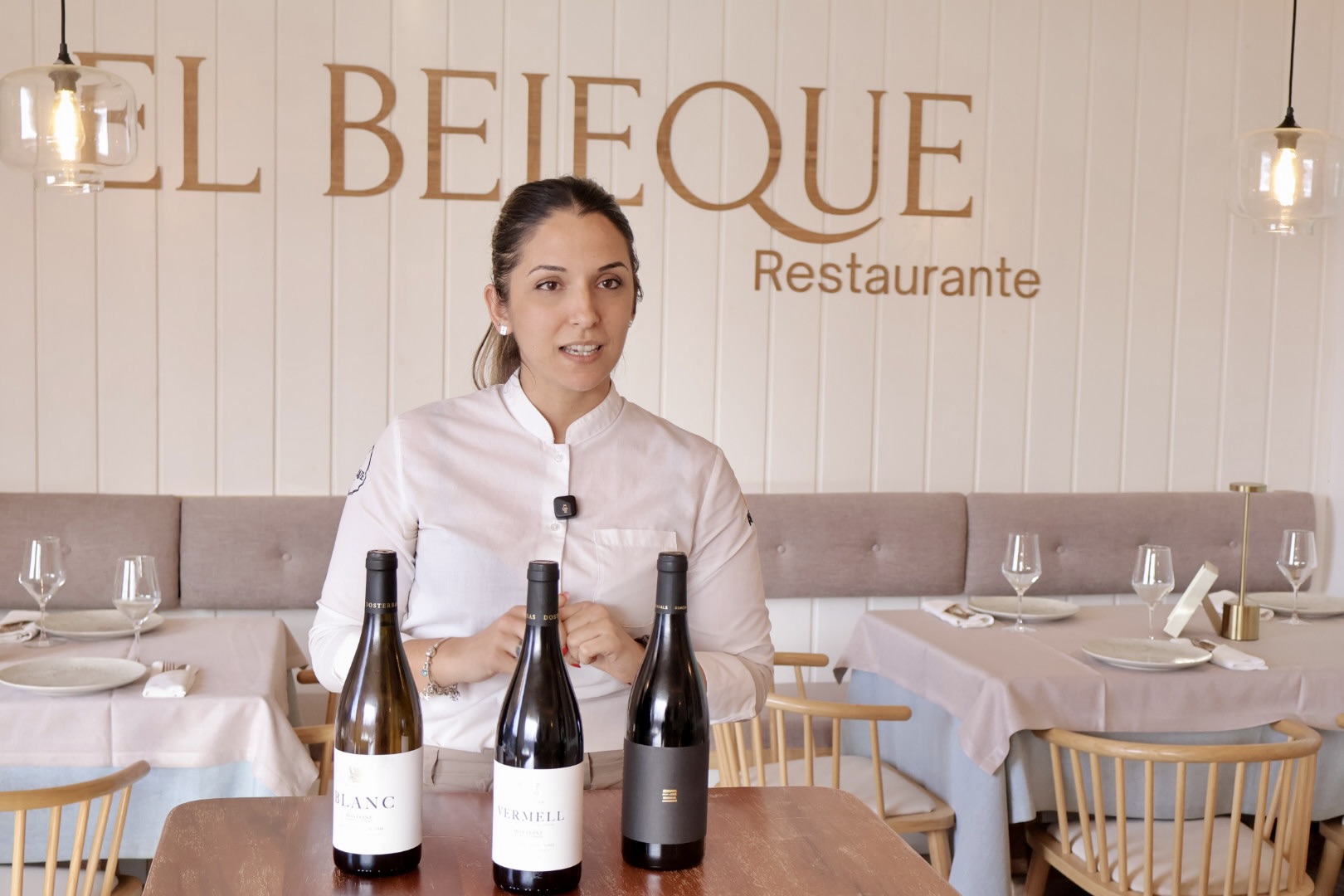 Kiara León en la sala de El Bejeque con tres botellas de vino y el rótulo del restaurante al fondo